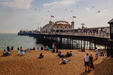 a group of people sitting at a beach with Brighton Pier Rock Shop in the background