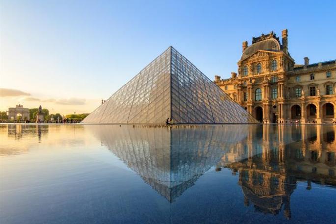 Louvre Pyramid and museum reflecting in water at sunset.