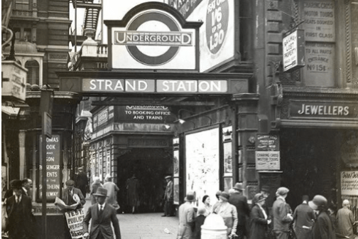 Vintage photo of busy street scene outside Strand Station, with people walking, signs, and advertisements.