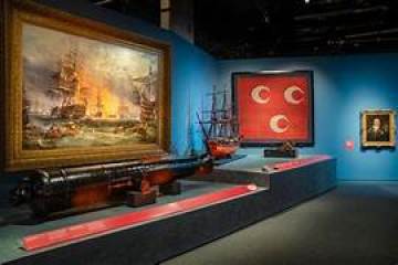 Museum exhibit with ship models, a naval battle painting, and a framed red flag with crescents Muslim Flag