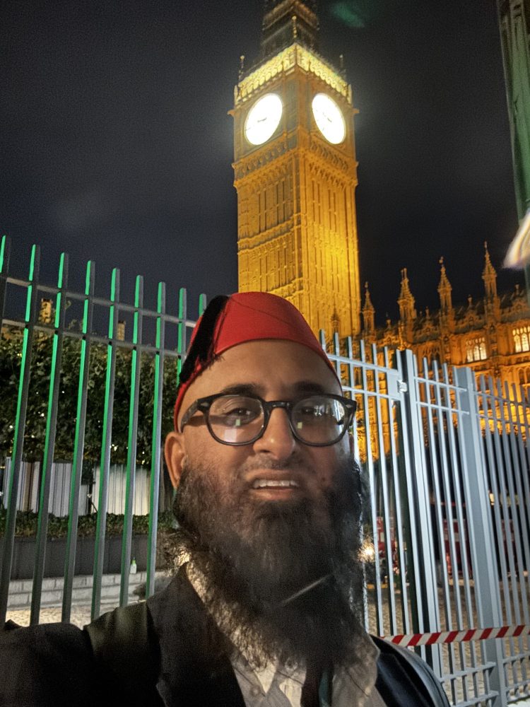 Person wearing a red hat and glasses smiling in front of Big Ben at night.
