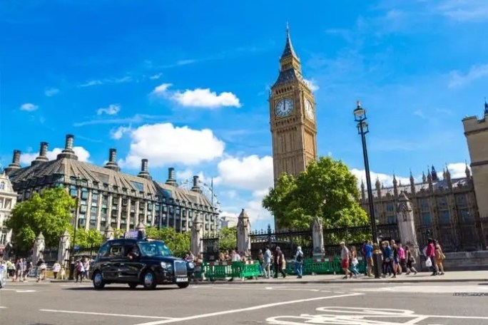 Street scene with Big Ben, cars, and pedestrians under a blue sky in London.