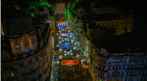 Aerial view of a festive street with colorful lights and crowded sidewalks at night.