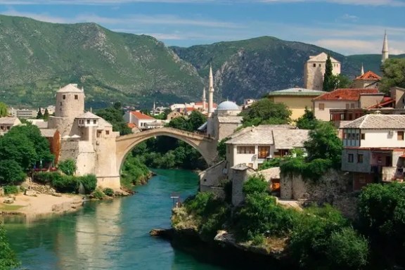 Historic stone bridge over a river with surrounding buildings and green hills.