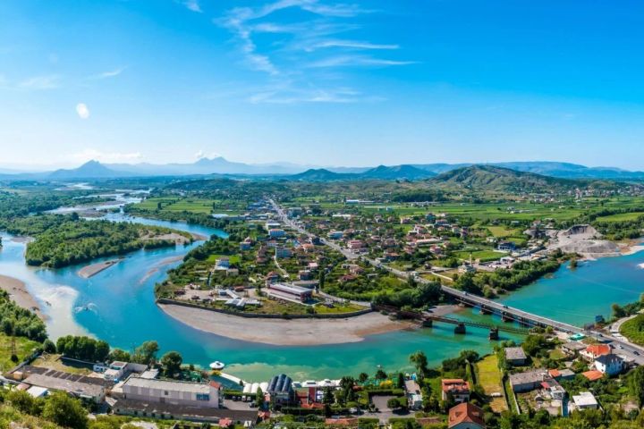 Aerial view of a river winding through a town with bridges and green landscapes.