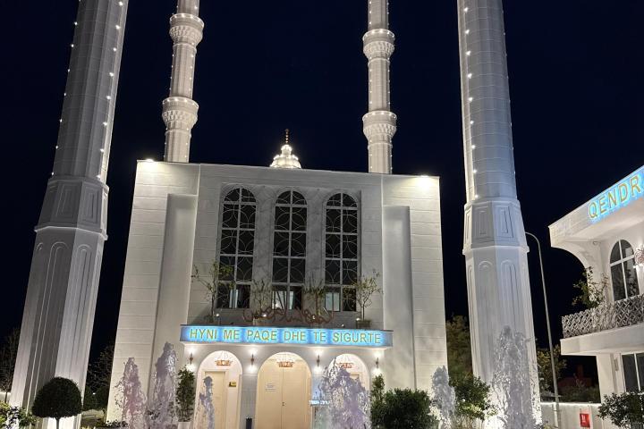 Illuminated mosque with tall minarets at night, colorful fountain in foreground.