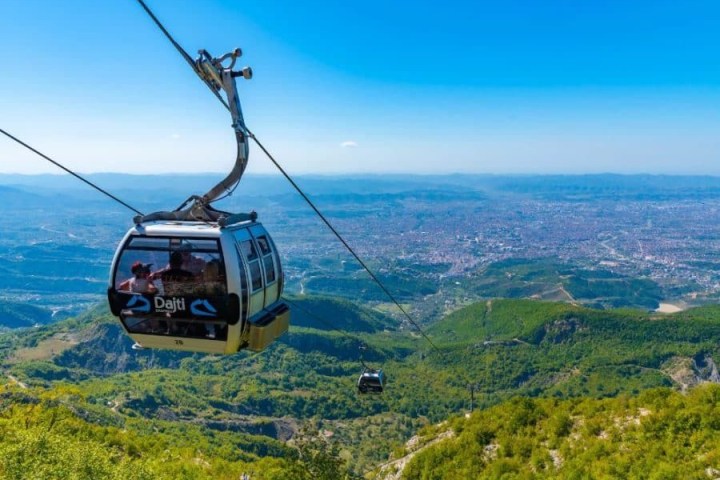 Cable car over green hills with a cityscape view on a clear day.
