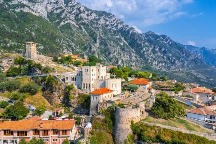 Scenic view of a hillside village with castle, red rooftops, and mountains.