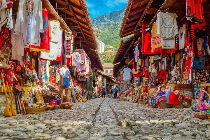 Cobblestone street lined with colorful clothing and souvenirs in an outdoor market.