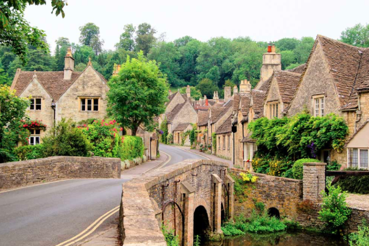 Quaint village street with stone cottages and green foliage.