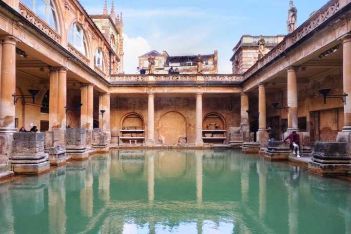 Historic Roman baths with columns, arches, and a green pool.