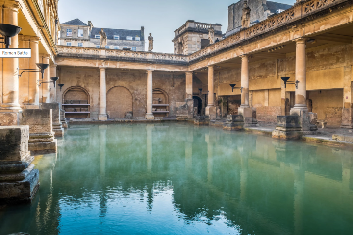 Historic Roman baths with columns, arched windows, and reflective greenish water.