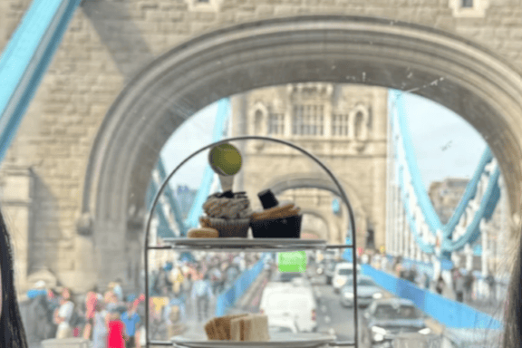 Afternoon tea setup with Tower Bridge view through a window, showing scones, sandwiches, and desserts.
