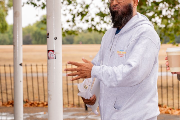 Man in glasses and hoodie holds coffee in park setting.