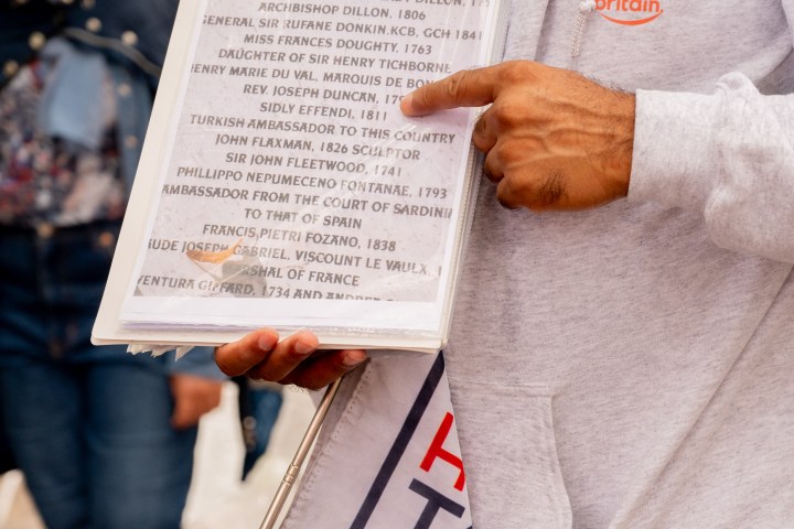 Person holding a sign with text and a brochure on a crowded street.