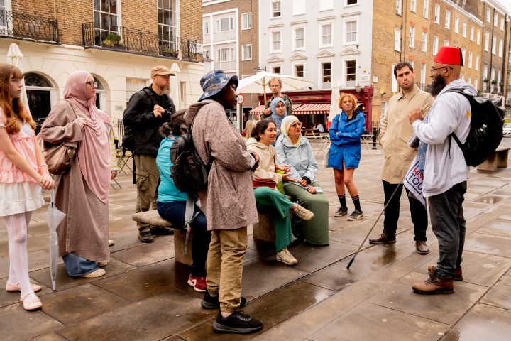 Group of diverse people listening to a guide on a city street.