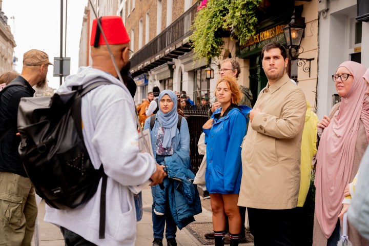 Group of people standing on a city street listening attentively.