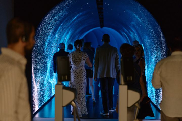 People walking through a blue-lit tunnel with sparkling walls.