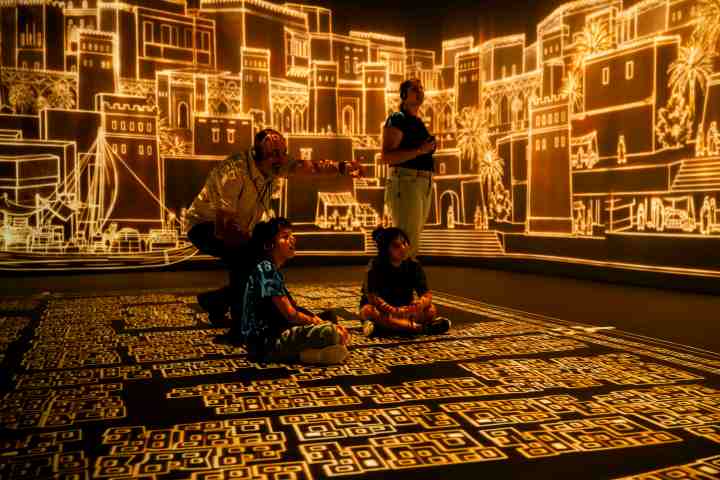 Four people view illuminated cityscape projections on walls and floor.