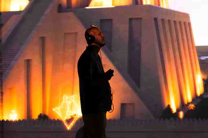 Person wearing headphones stands before lit, pyramid-like structure.