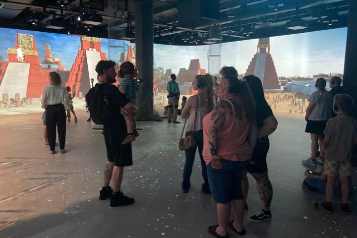 People viewing immersive exhibit with projected ancient structures.