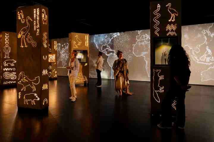 People exploring illuminated displays with ancient symbols in a dimly lit exhibition space.