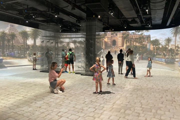 People interact with immersive historical city projections on walls and floor.