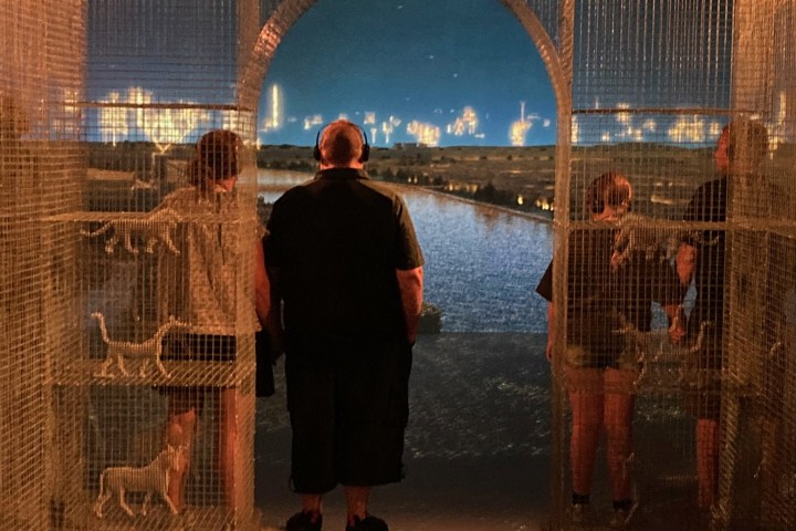 People stand in a lit archway, overlooking a nighttime waterfront.