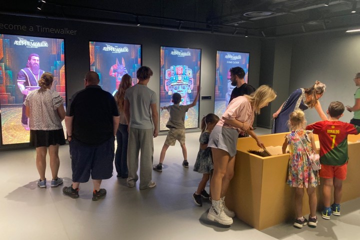 People interacting with digital screens and a table in a modern exhibit space.