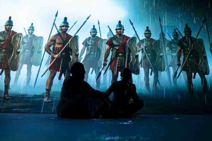 Silhouettes of two people sitting, surrounded by soldiers in ancient Roman gear.