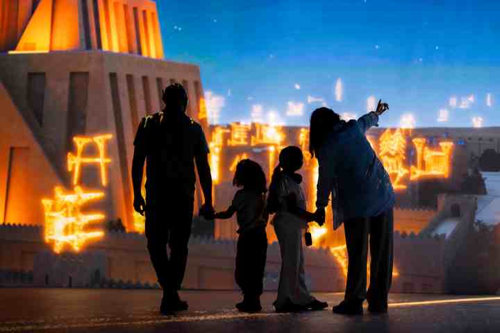 Silhouetted family watches illuminated ancient building display.