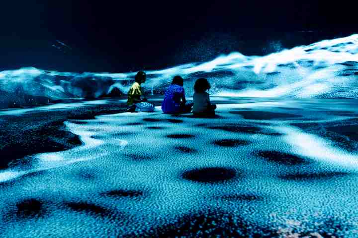 Three children sit on a floor with blue and white swirling pattern