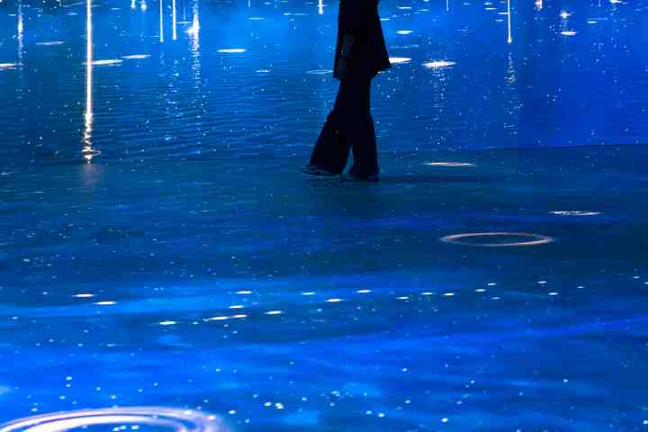Person standing in immersive blue digital art exhibit with light streaks and water-like effects.