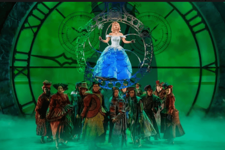 Theatrical scene with woman in blue gown above group under green-lit clock.